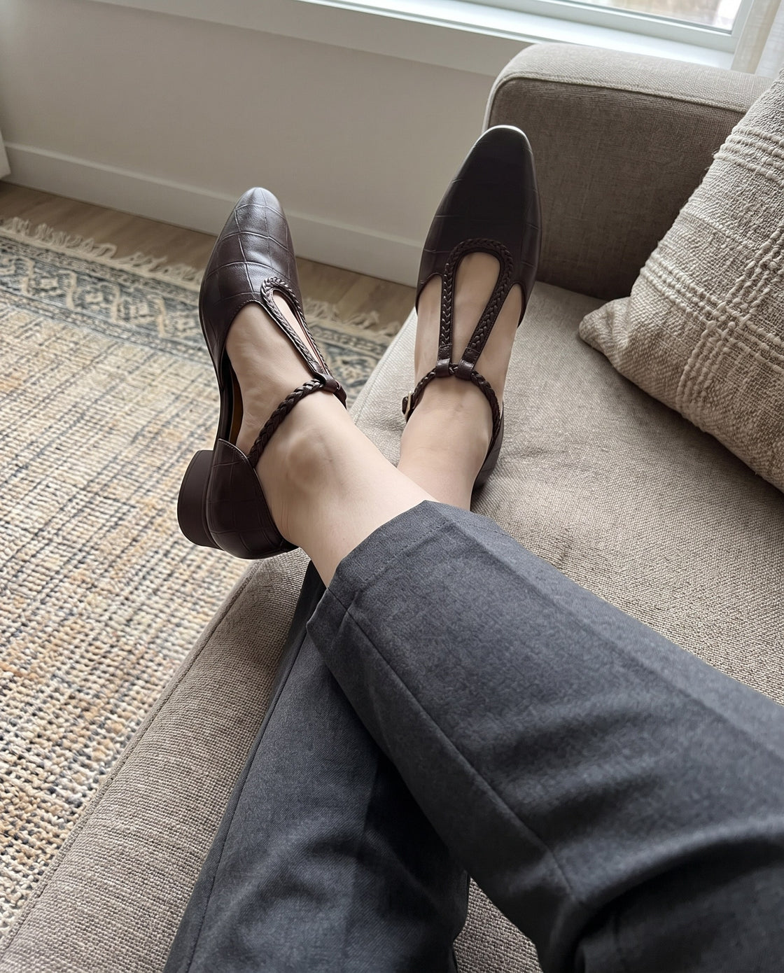 Brown shoes with a braided strap, feet resting on a sofa